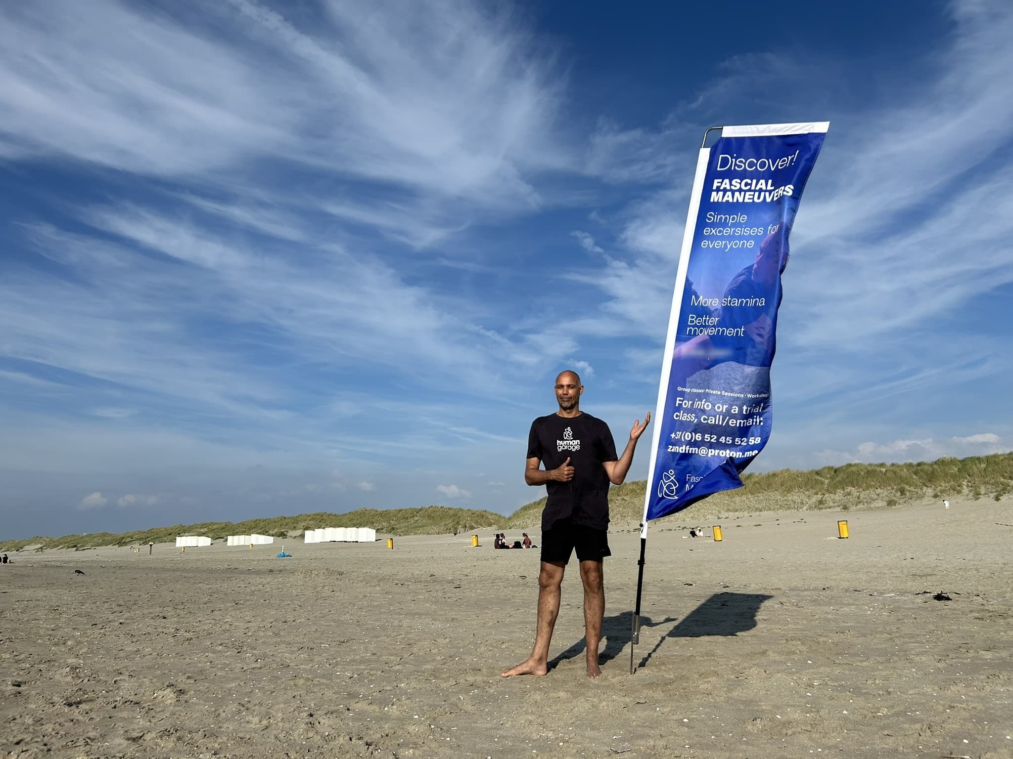 Rene Zand on the beach beside his Fascial Maneuvers banner